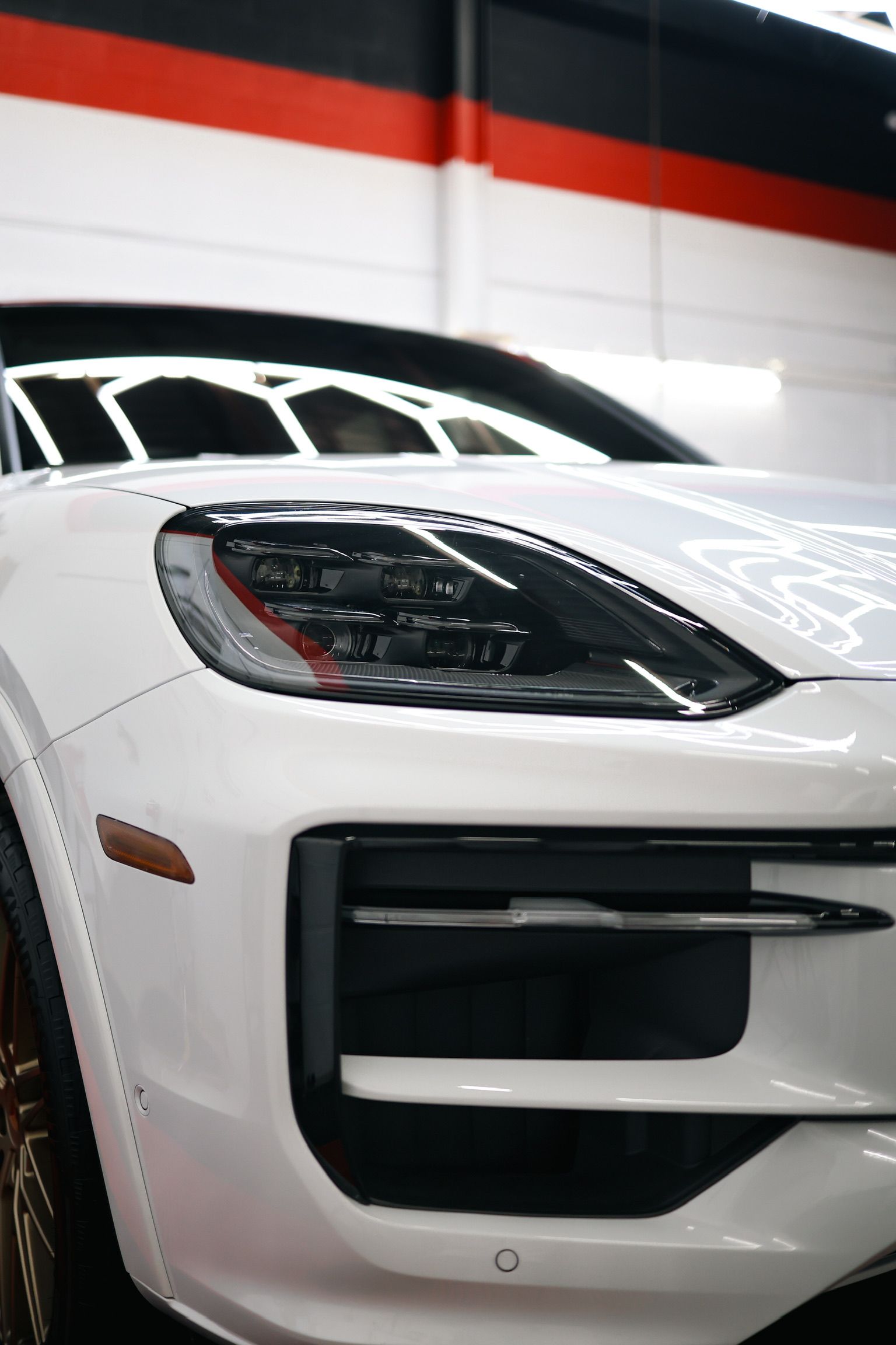 White car with gold rims on a red and black floor, against a white and black wall.