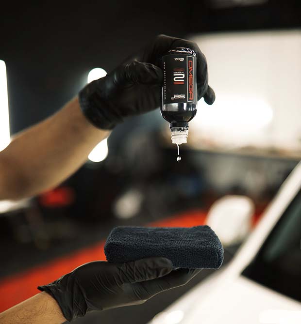 A person wearing black gloves is holding a bottle of liquid and a sponge