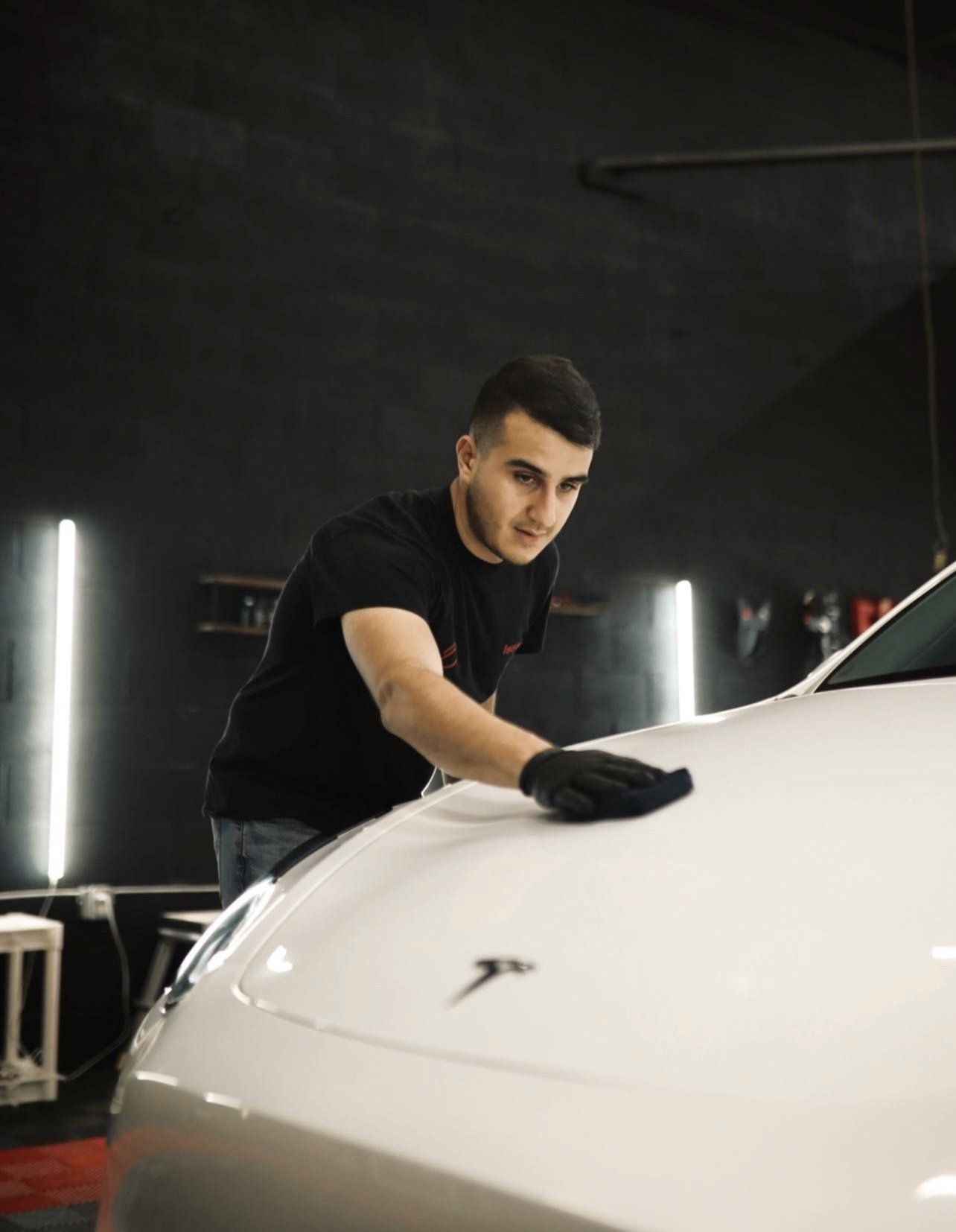 A man is cleaning the hood of a white tesla model 3.