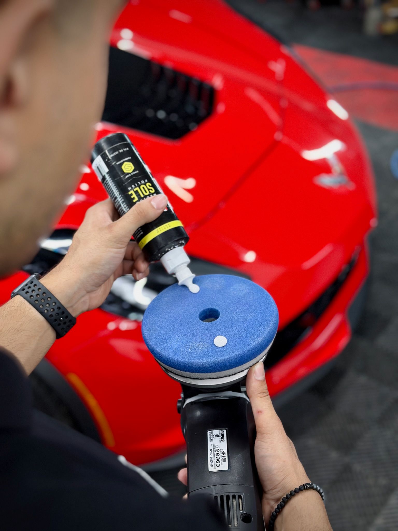 A man is polishing a red car with a polisher