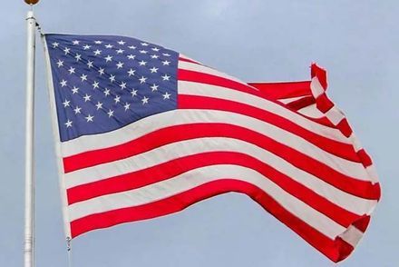 An American flag flying on a pole against a light blue, cloudy sky.