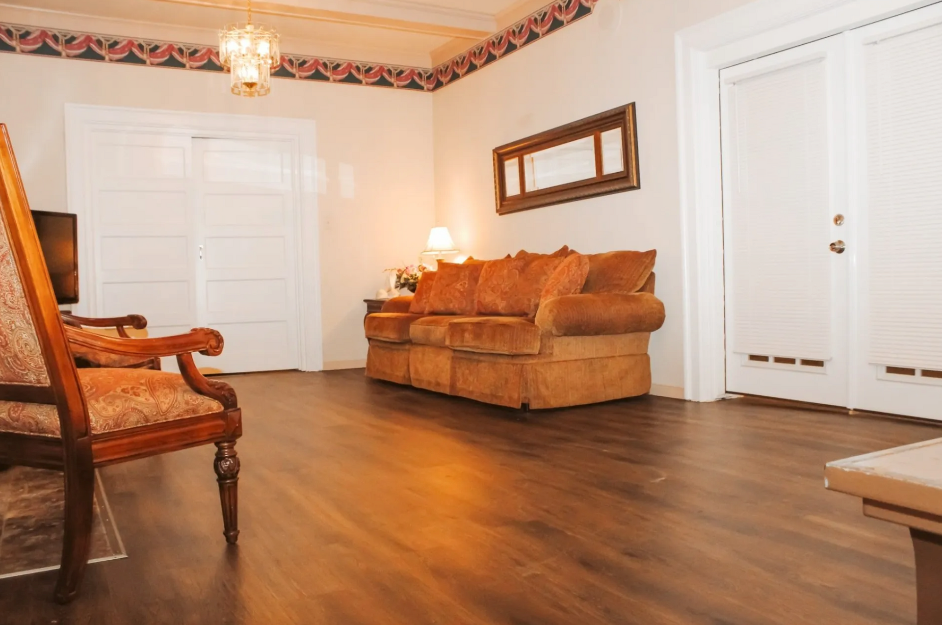 Empty living room with brown sofa, wooden chair, white doors, and hardwood floor