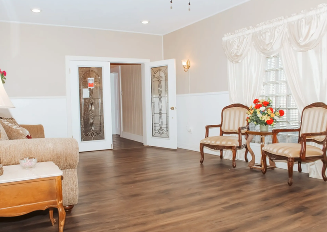 Bright living room with wood floors, wicker chairs, floral curtains, and open double doors