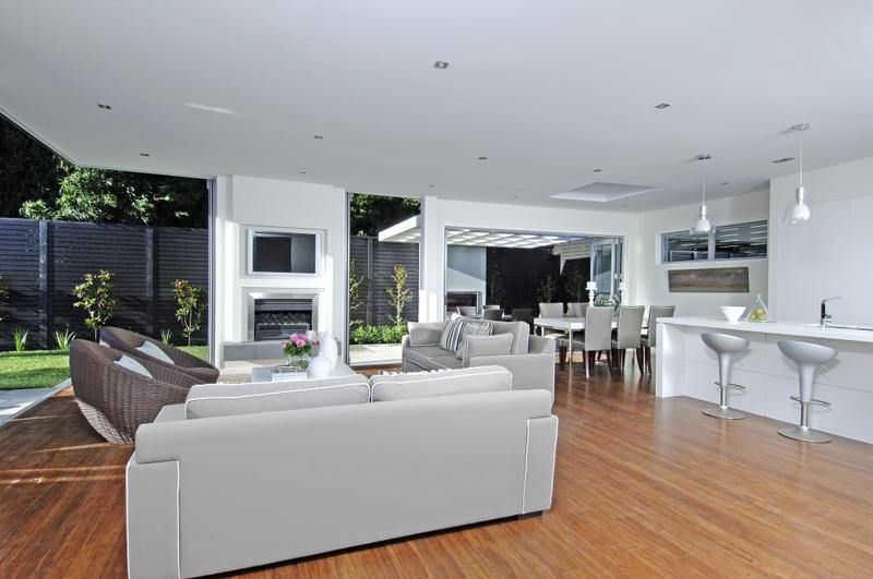 Modern open-plan living room with white sofas, fireplace, and dining area, opening onto a patio.