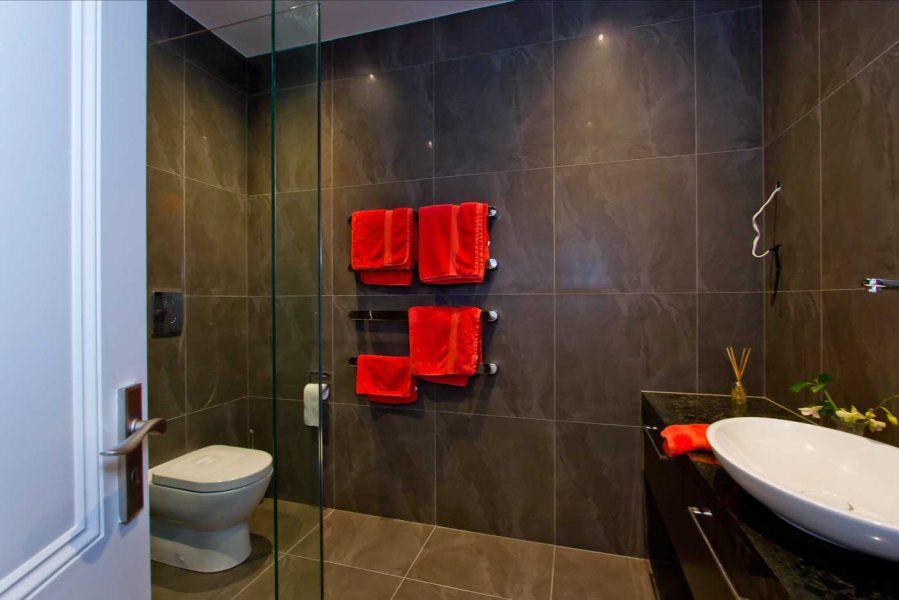 Bathroom with gray tiled walls, red towels on a heated rack, and a white sink.