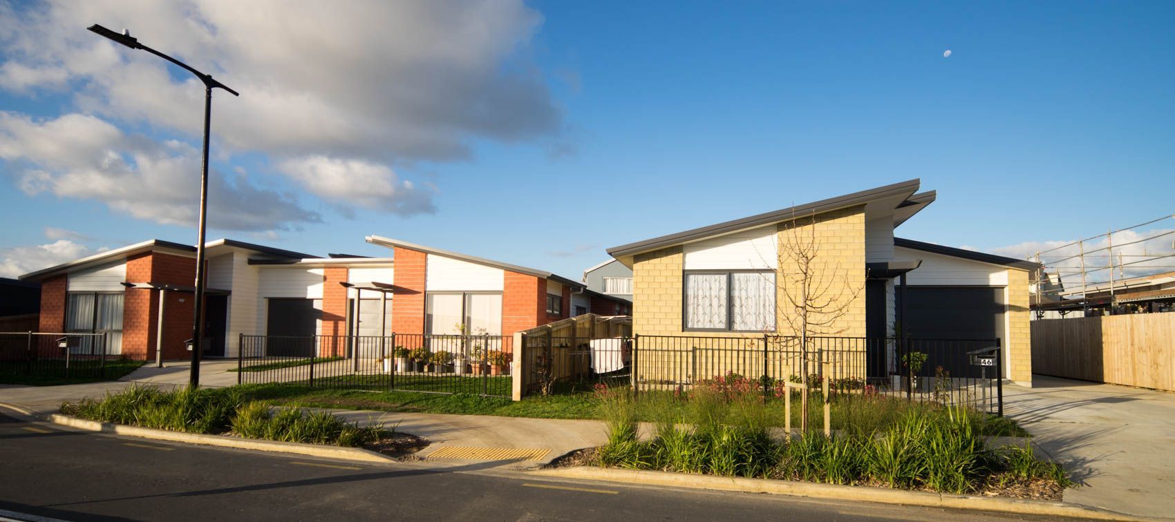 Two modern homes with angled roofs and a grassy area under a blue sky with clouds.