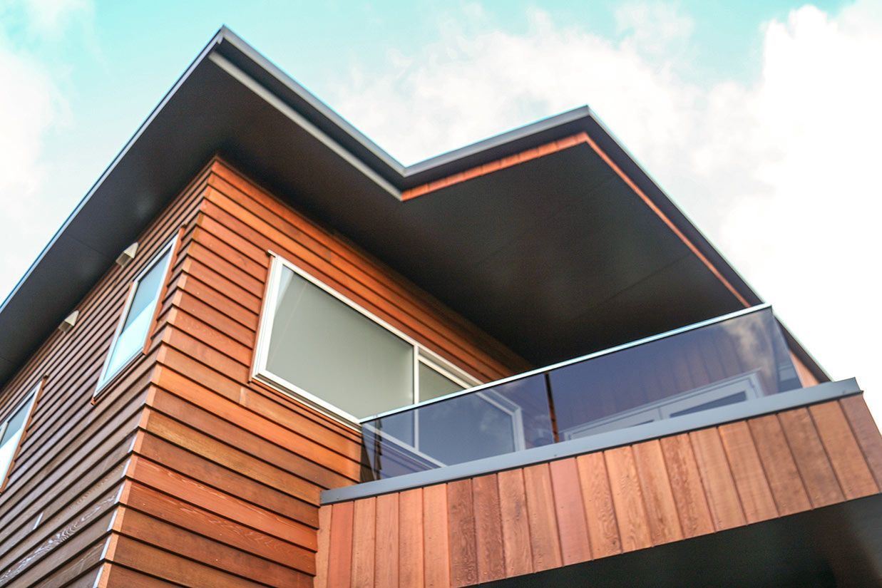 Modern house exterior with wood siding, a dark roof, and a glass balcony railing.