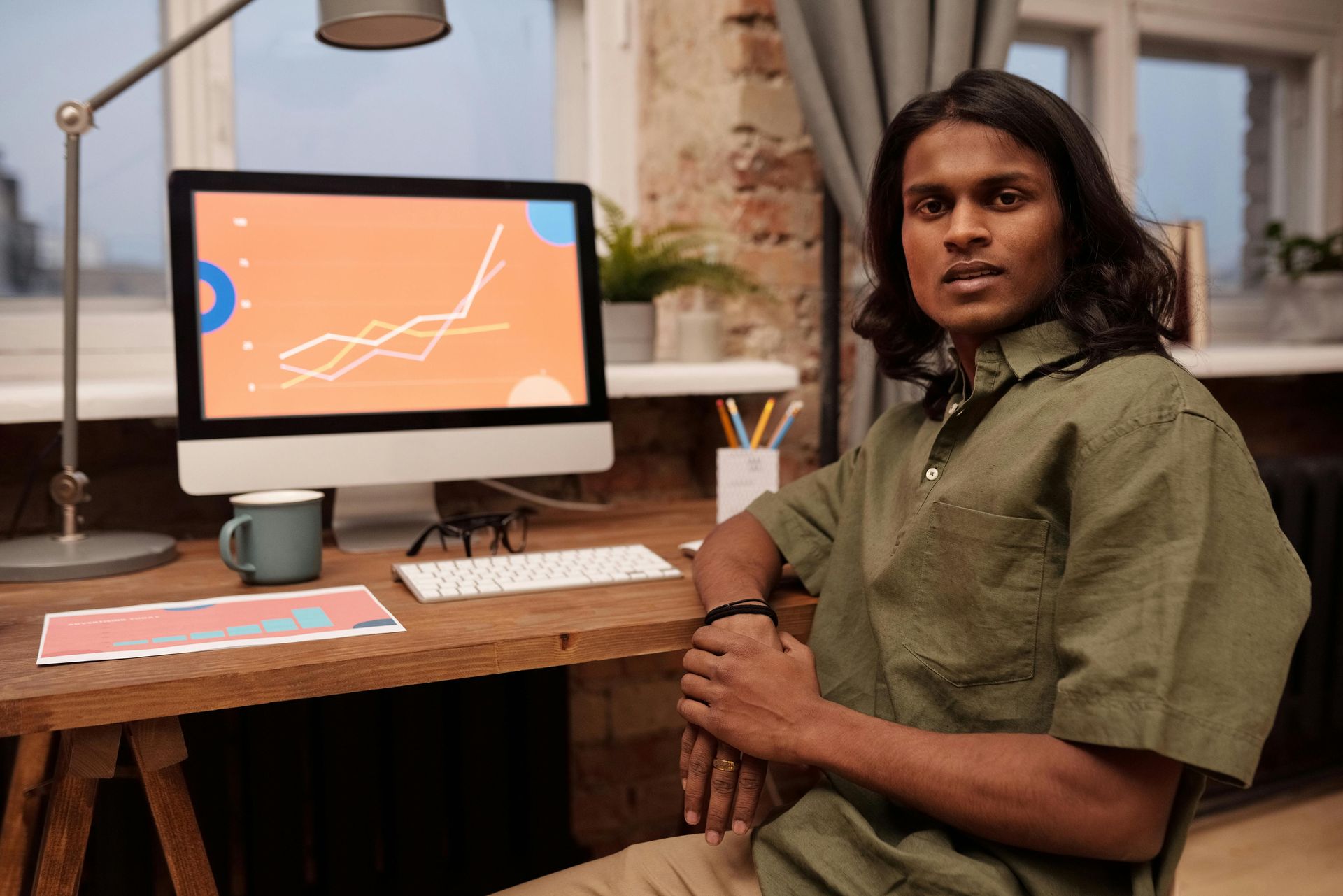 Man sitting at a desk, looking at the camera. A computer with orange graphics is in front of him.