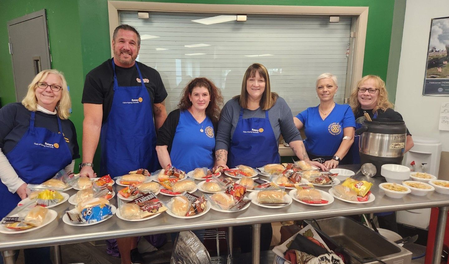 A group of people are standing around a table filled with food.