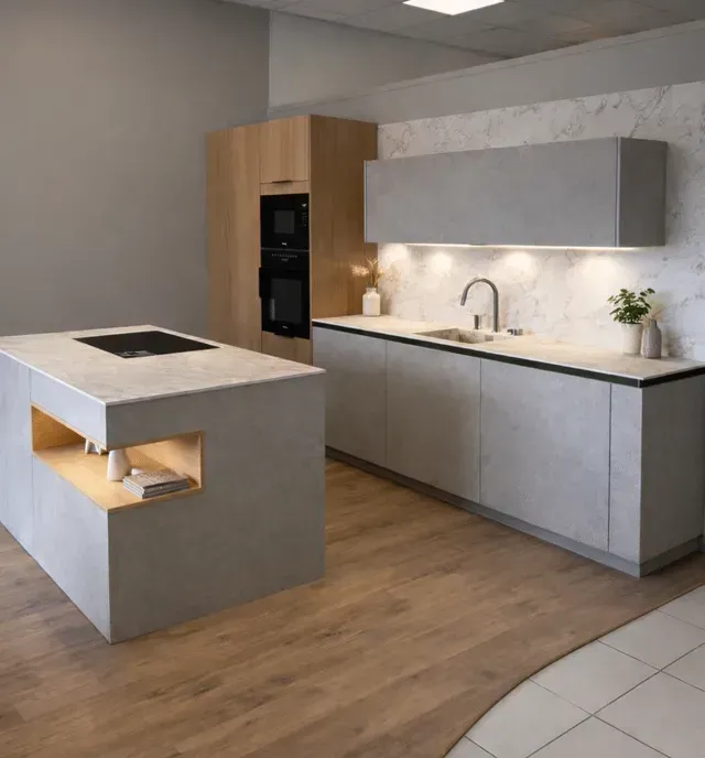Cuisine moderne avec armoires grises, parquet, îlot central avec plaque de cuisson et four encastré noir