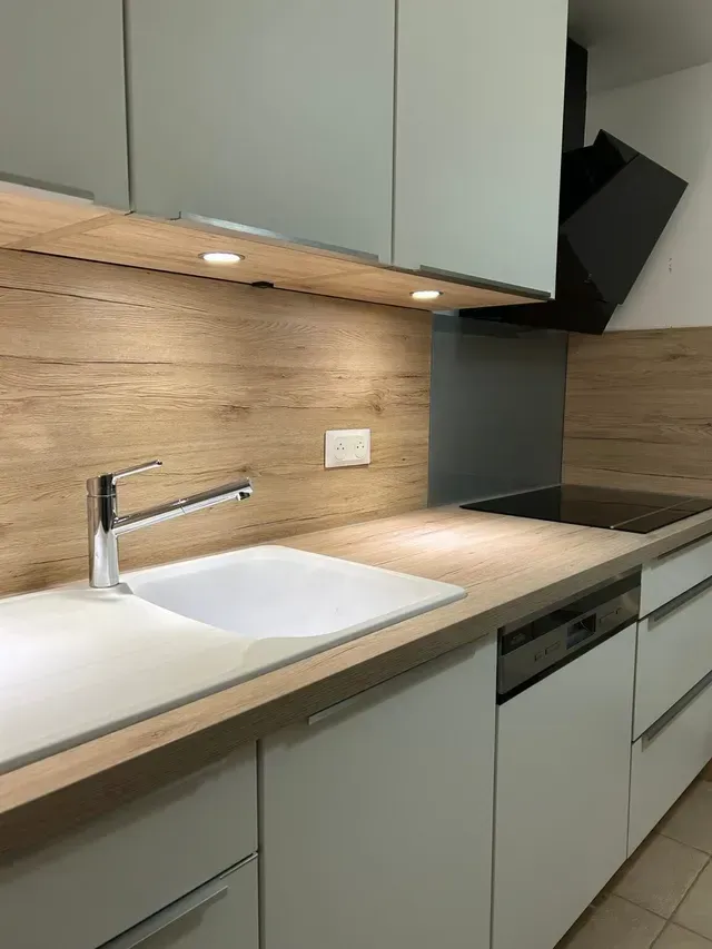 Cuisine moderne avec placards clairs, crédence en bois, évier, plaque de cuisson et four intégrés