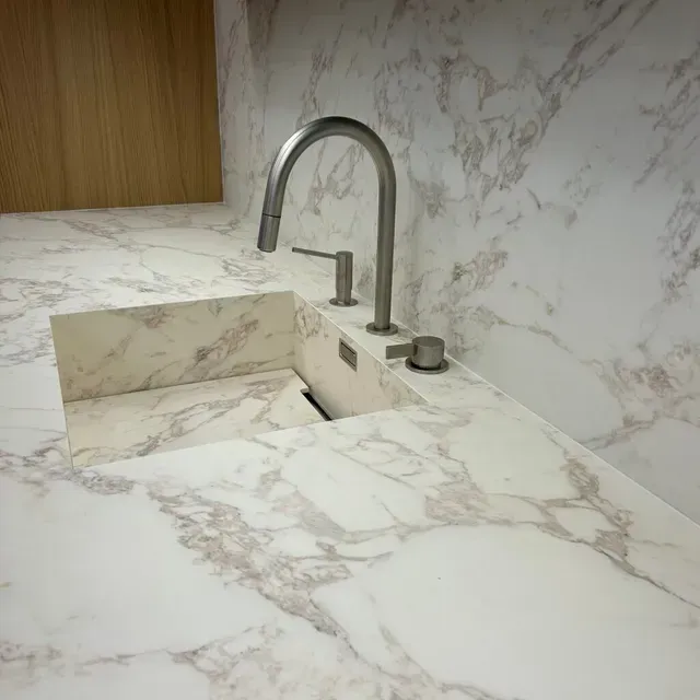 Plan de travail en marbre avec lavabo intégré et robinet chromé incurvé dans une salle de bain ou une cuisine moderne