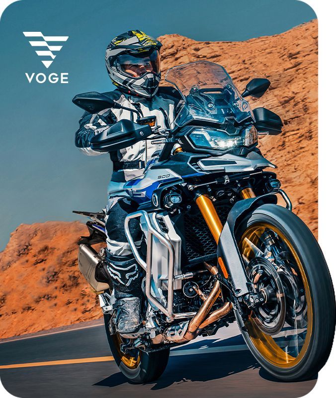 Motociclista pilotando uma moto esportiva azul em uma estrada deserta com penhascos alaranjados ao fundo.