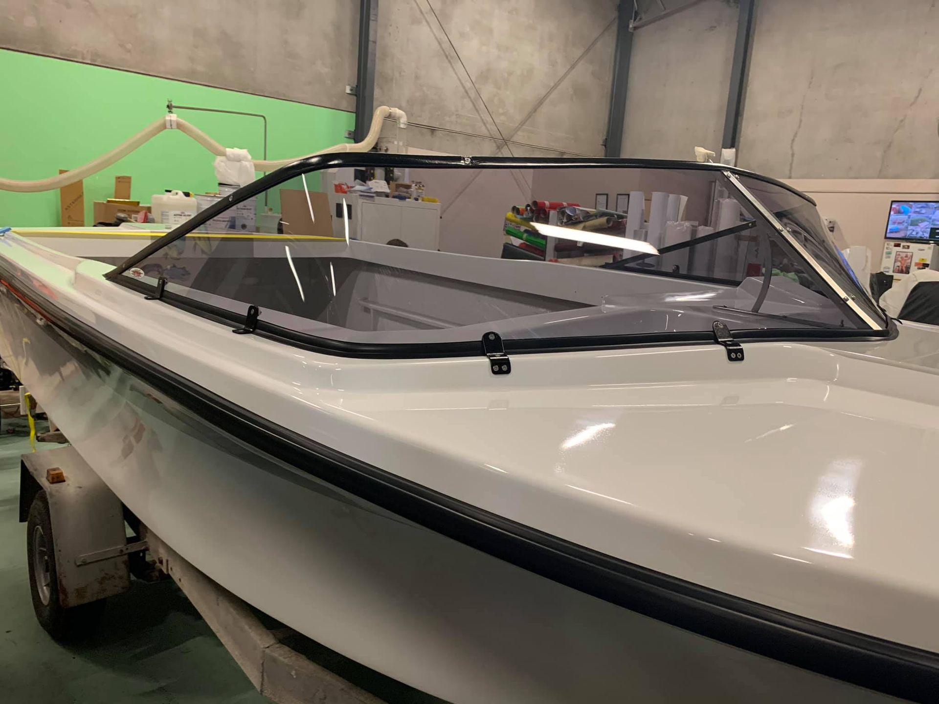 A white boat with a windshield is sitting in a warehouse - Plastiglass Mid North Coast, NSW