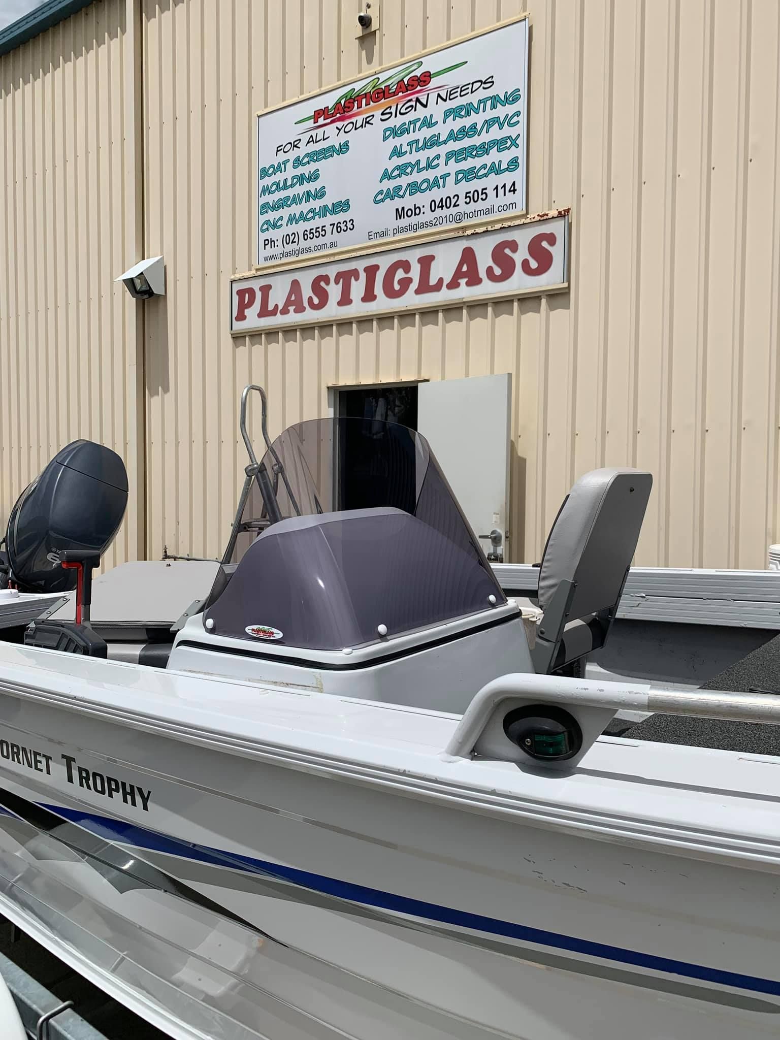 A boat is parked in front of a building with a sign that says plastiglass - Plastiglass Mid North Coast, NSW