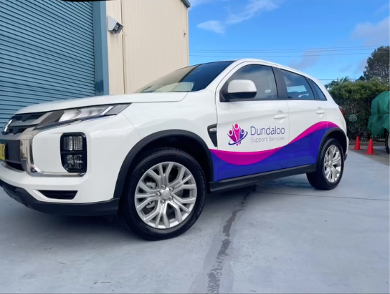 A white car with a purple logo is parked in a parking lot - Plastiglass Mid North Coast, NSW