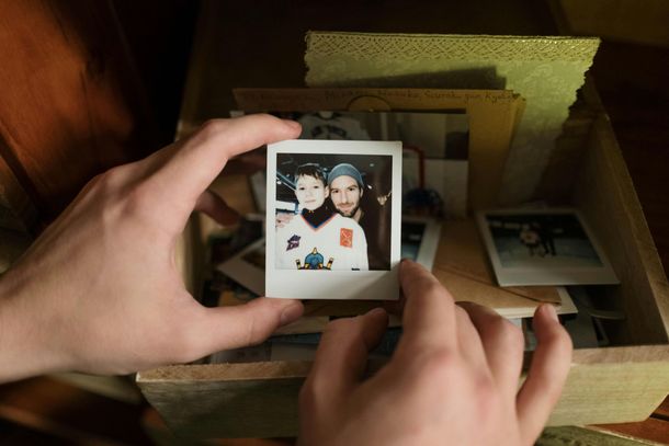 Hands holding a Polaroid photo over a box of stacked photographs in warm light