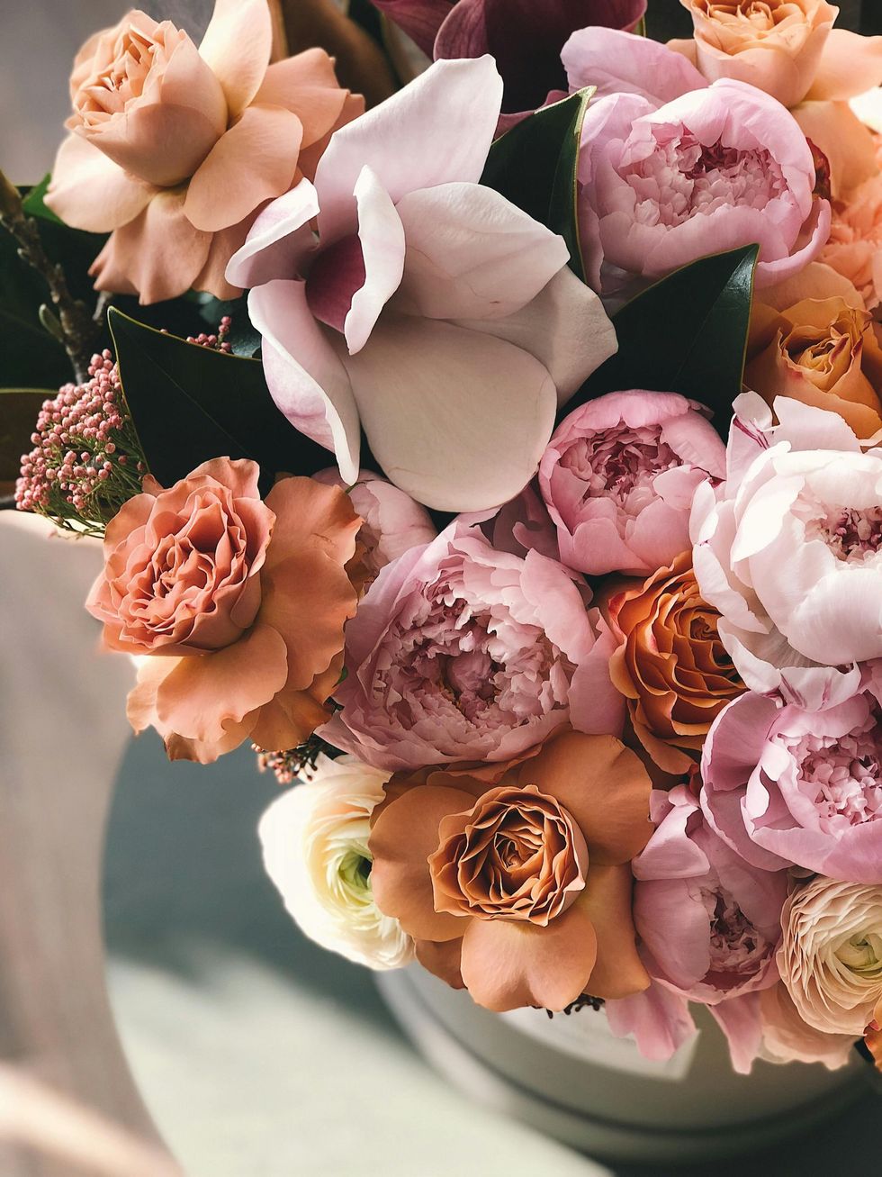 Bouquet of pastel pink, peach, and cream roses arranged in a white vase