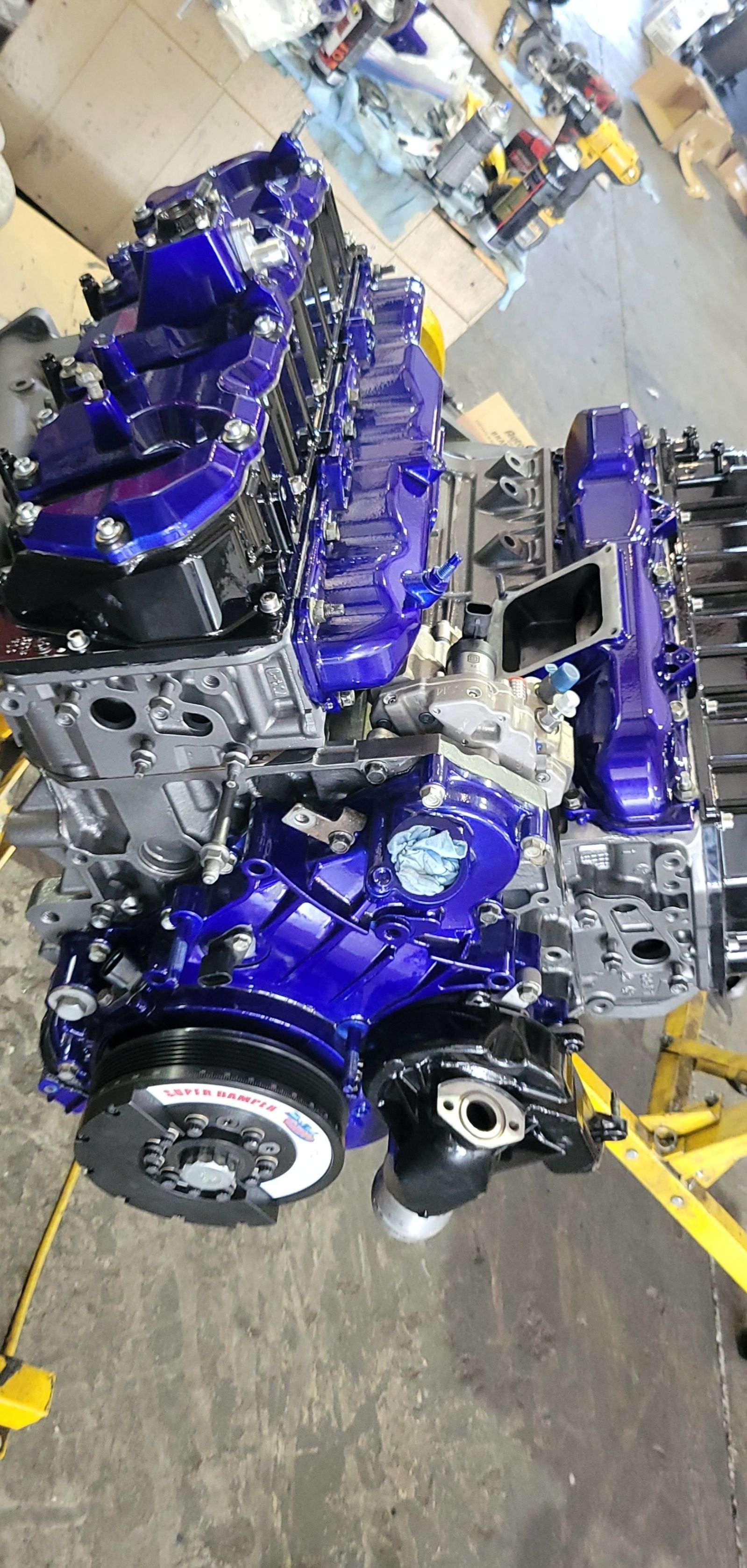 A blue engine is sitting on top of a yellow lift in a garage.