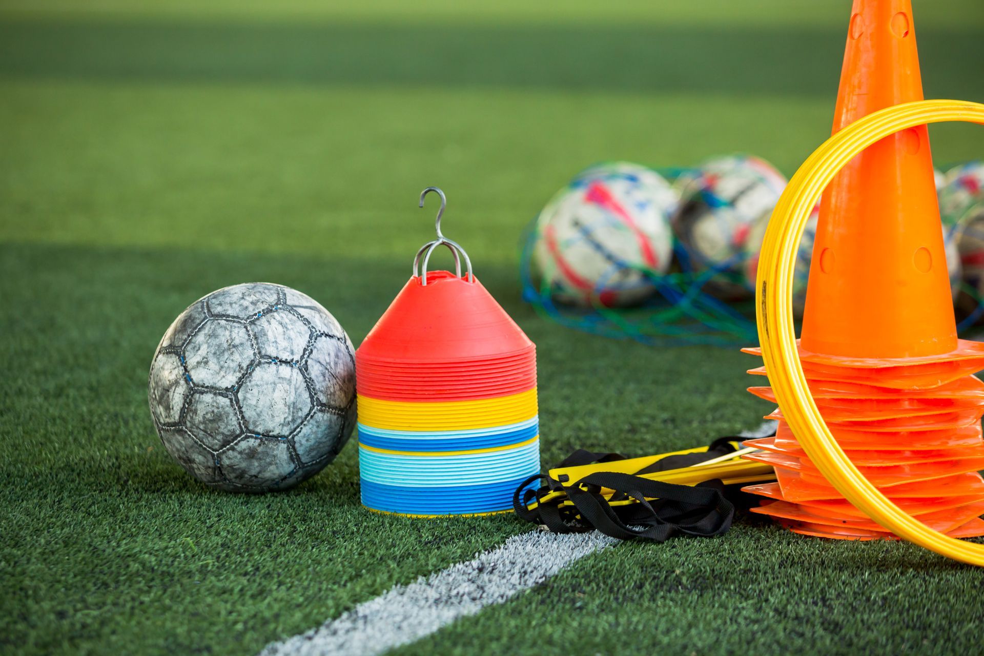 Soccer training gear on turf: cones, agility hoop, balls, and a rainbow-striped marker box.