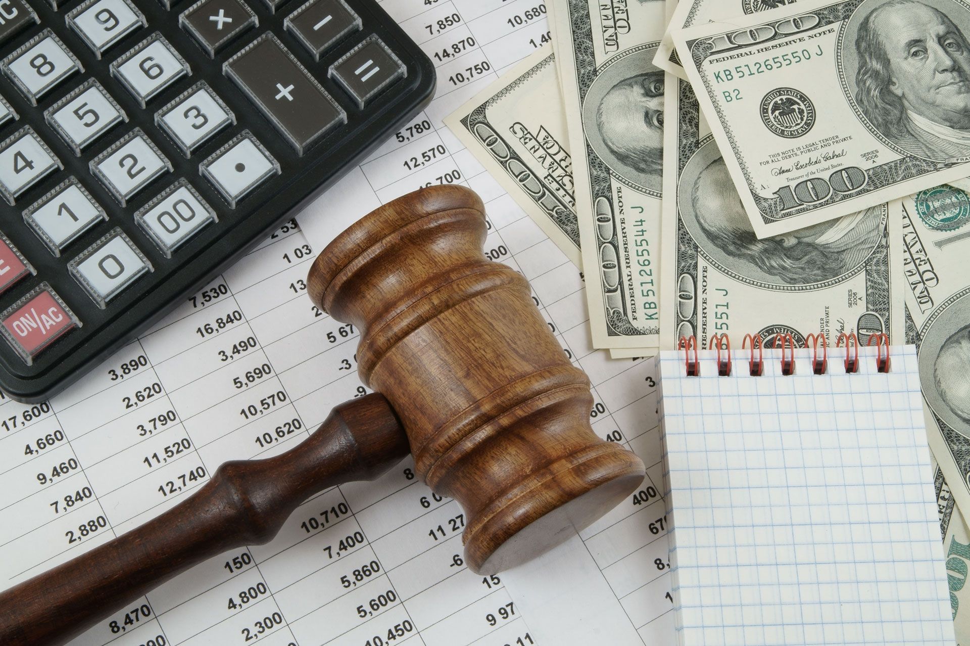 Judge’s gavel beside calculator, U.S. dollar bills, and paperwork on a desk
