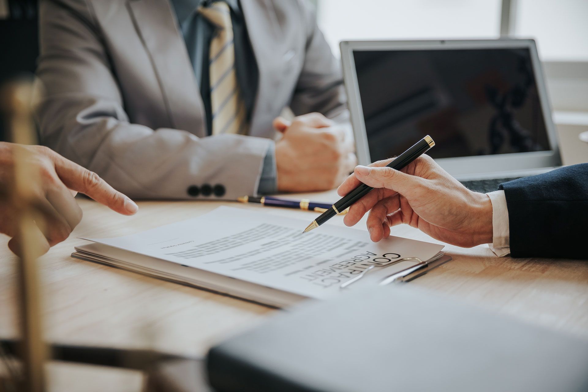 People in business attire reviewing documents and signing a contract at a conference table with a laptop nearby