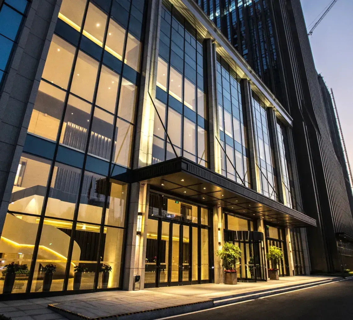 Modern glass office building at dusk with illuminated lobby and curved façade