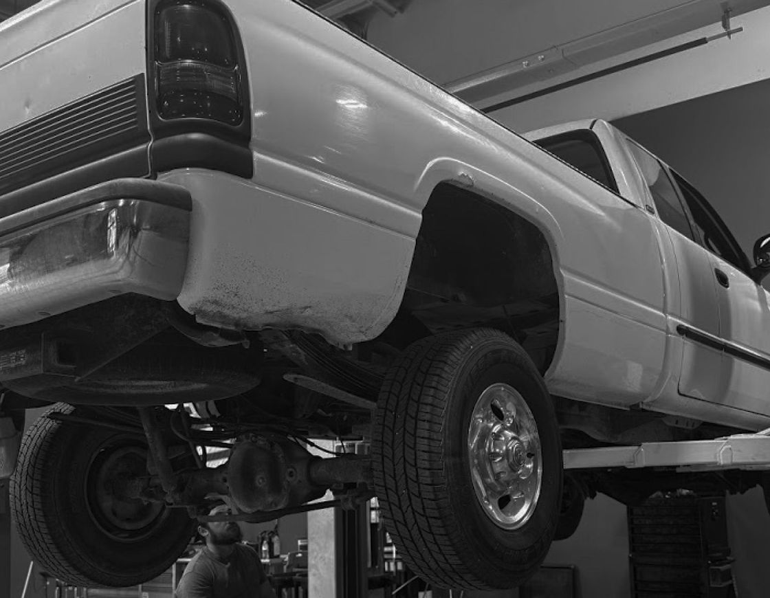 White pickup truck lifted on a garage lift, viewed from the rear-left underside. | G3 Transmission and Auto