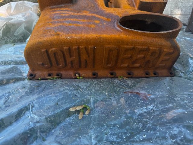 Rusty John Deere tractor part on a tarp, with the brand name visible.