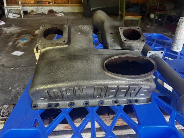 Gray John Deere air intake manifold on a blue crate, showing lettering and openings.