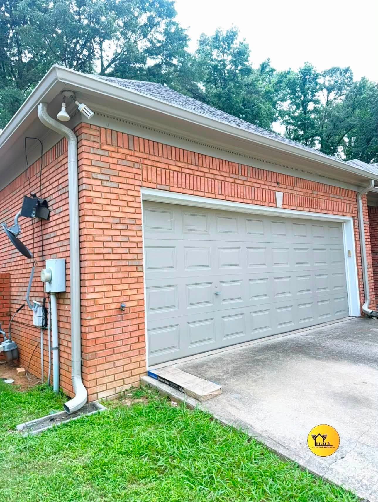 Brick house exterior with a closed white garage door, gutter downspout, and concrete driveway.
