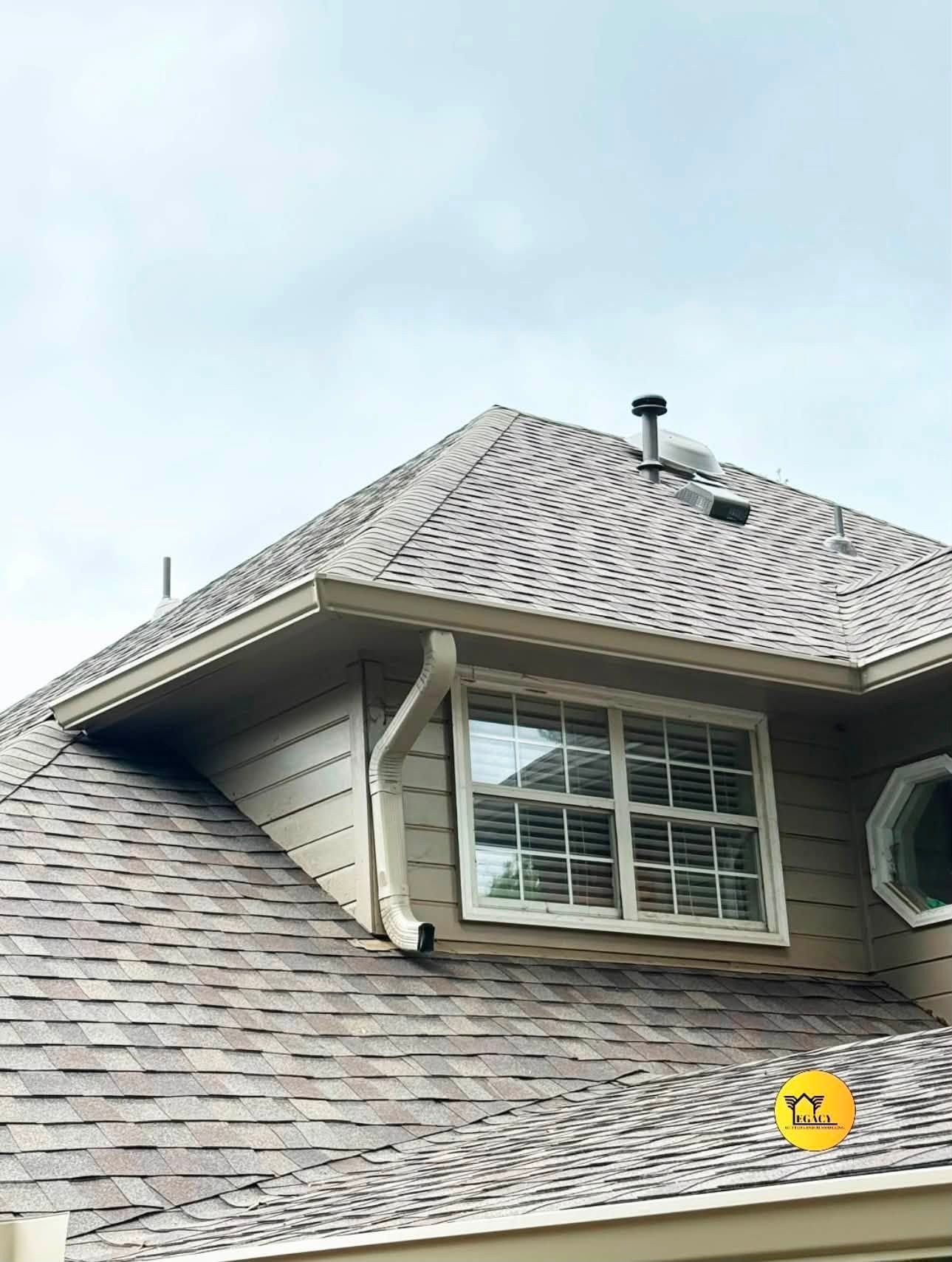 Gabled house roof with gray shingles and a dormer window under a cloudy sky