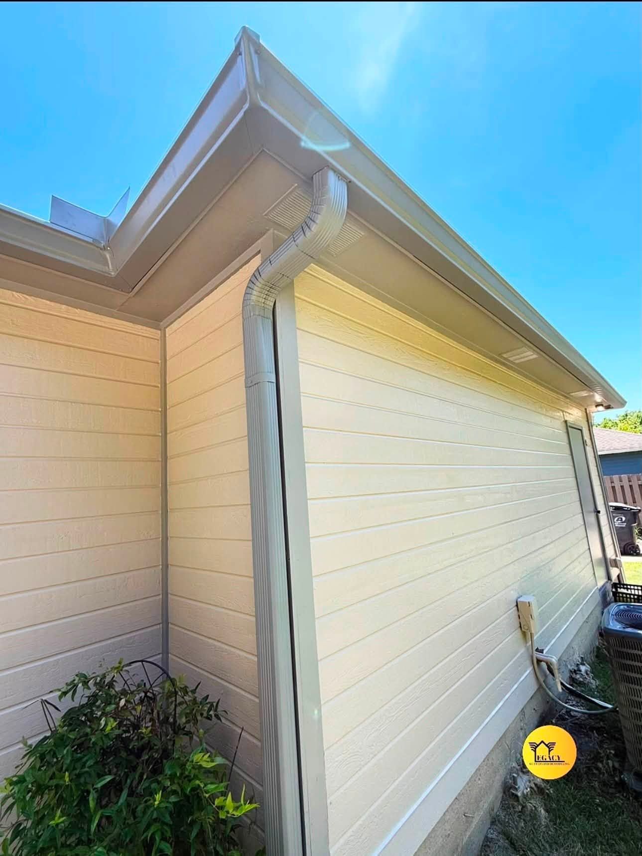 Beige house exterior corner with gutter and roof eaves under a blue sky.