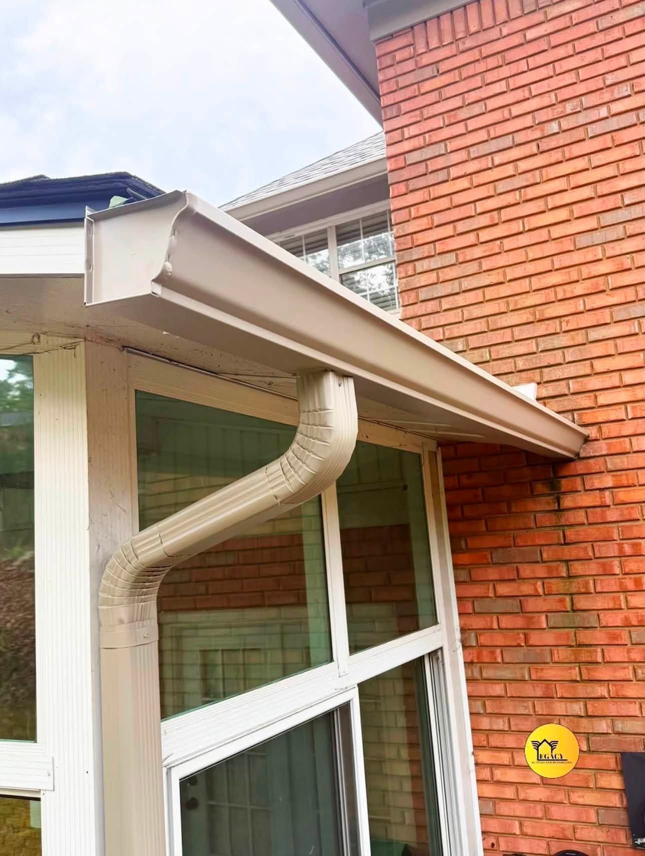 White downspout on brick house beside a slanted roof and window under a blue sky