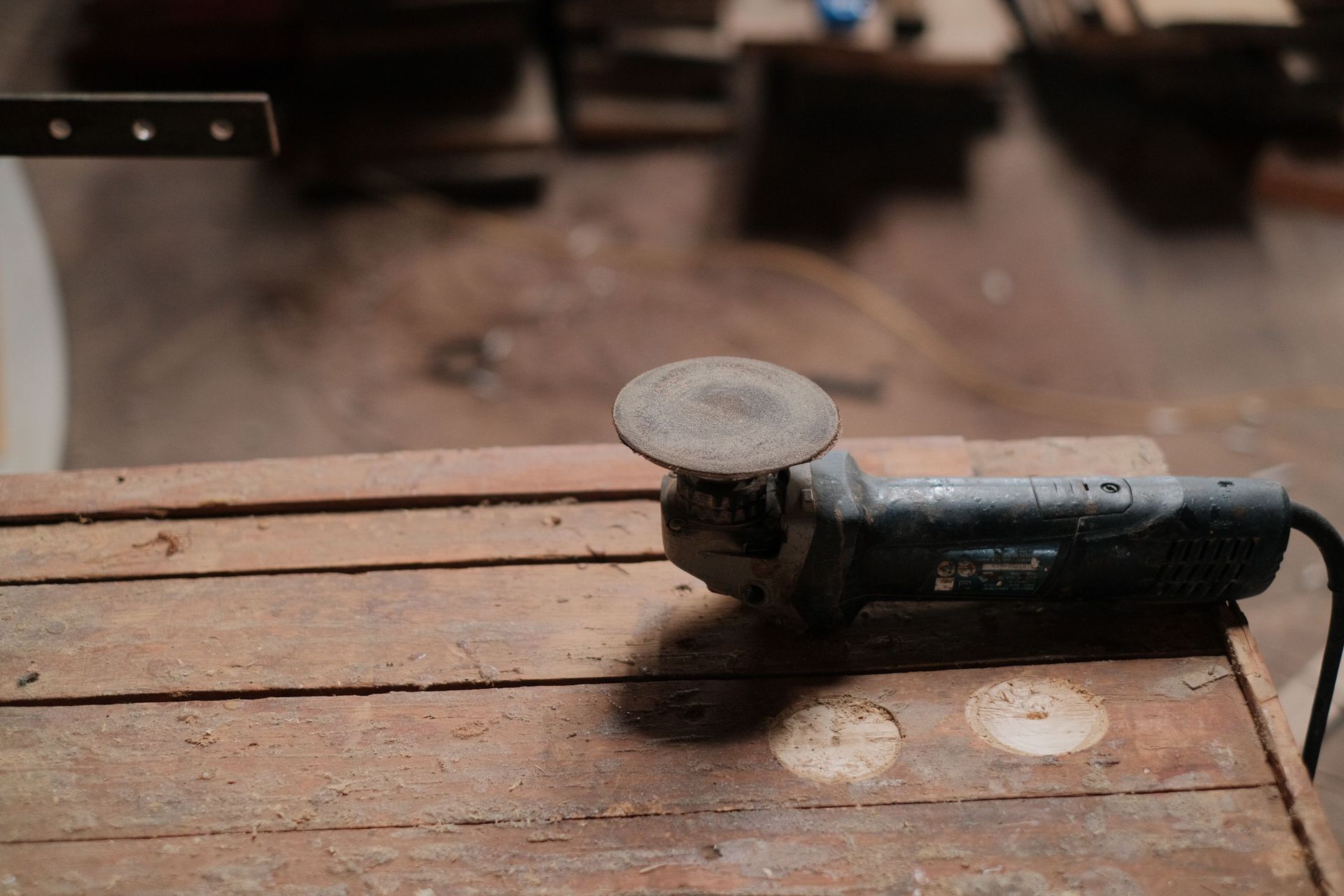Angle grinder resting on a wooden workbench, with a blurred workshop background