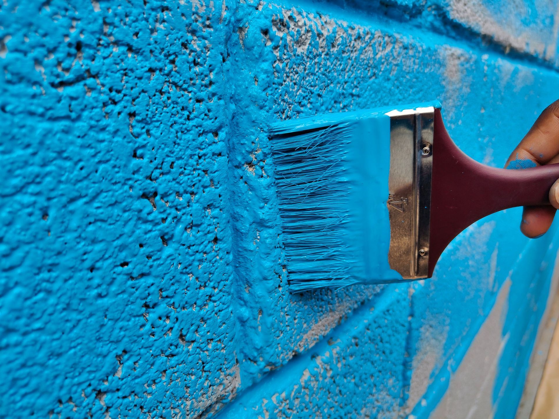 Paintbrush applying bright blue paint to a textured wall