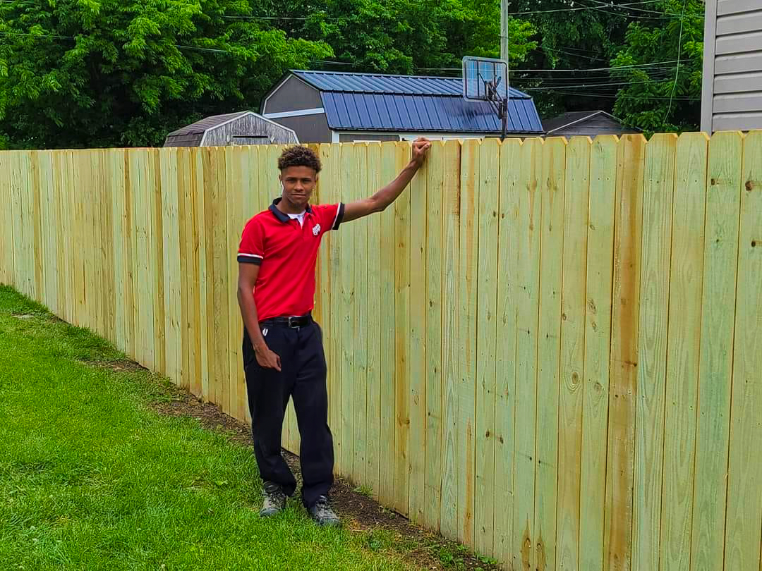 Red Beaver Construction team member standing next to a completed fence project.