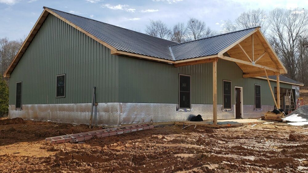Rural pole barn under construction by Red Beaver Construction, with large wooden posts being set into the ground, workers building, and construction equipment.