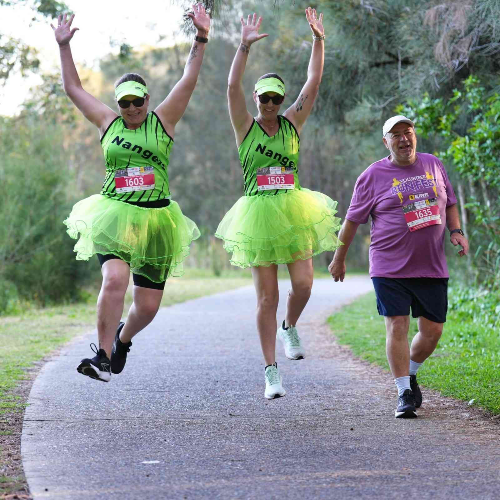 Two Women in Green Tutus Jump for Joy as They Run a Race, a Man Jogs Alongside — Run Fest in Central Coast, NSW
