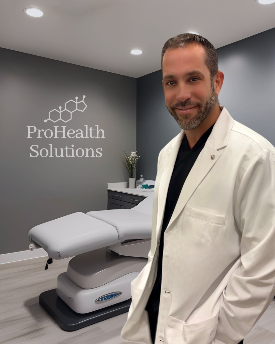 Doctor in a white coat stands next to an examination table in an office. 