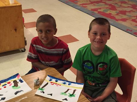 Two young boys are sitting at a table with paintings on it