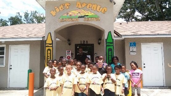 A group of children standing in front of a building that says kids avenue