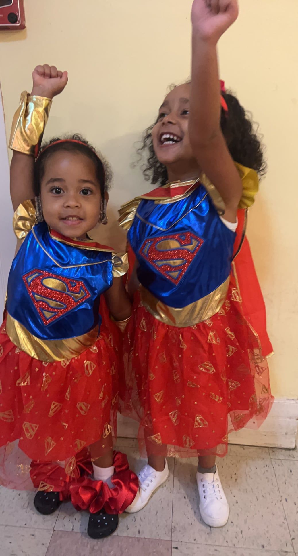 Two little girls dressed in superman and wonder woman costumes are standing next to each other.