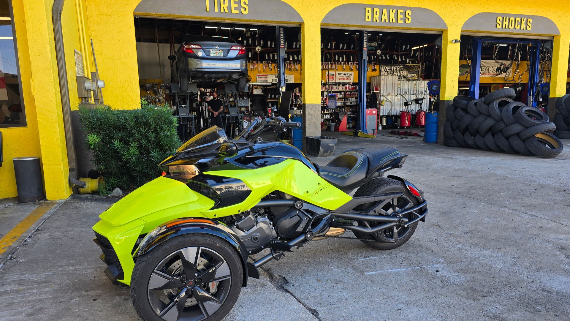 Neon green Can-Am Spyder motorcycle parked in front of a yellow garage with 