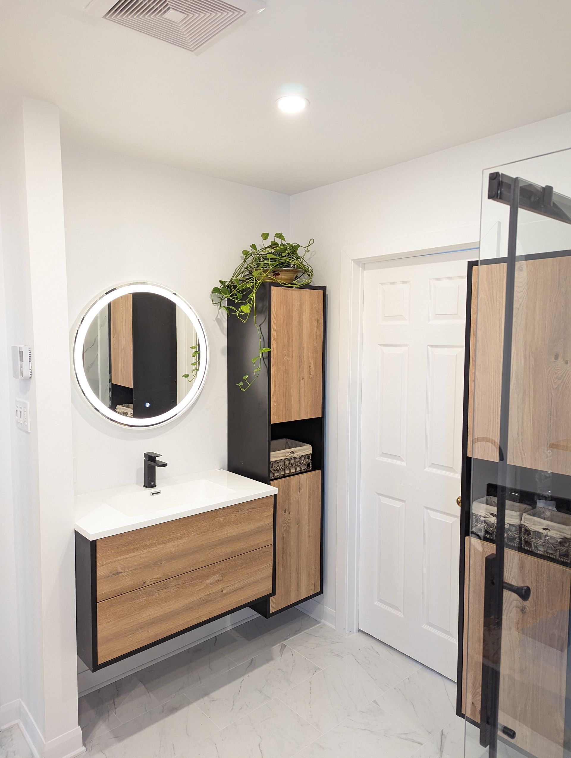 Salle de bains moderne avec murs blancs, meubles en bois et miroir rond.
