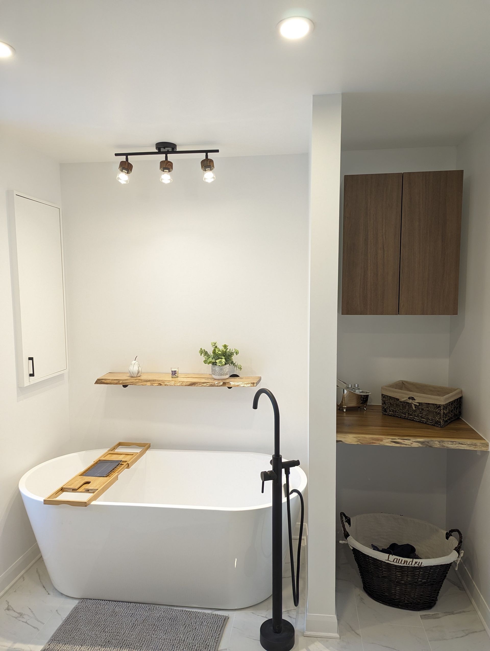 Salle de bains moderne avec douche à l'italienne, robinetterie noire et meuble de rangement couleur bois. Murs blancs et carrelage imitation marbre.