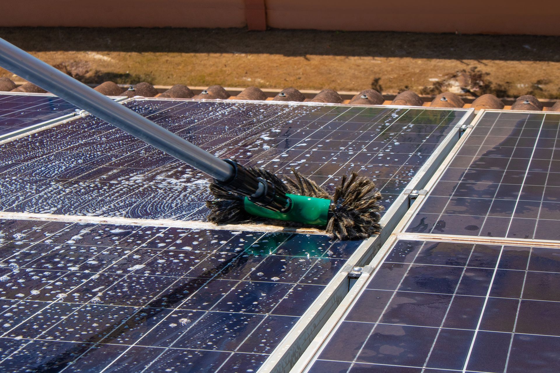 A close-up of a solar panel being cleaned with foamy, white soap suds on its blue, gridded surface.