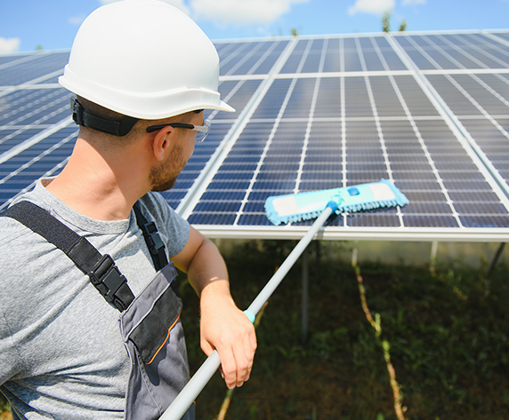 A cleaning tool with a squeegee head being used to wash a dark-colored solar panel.