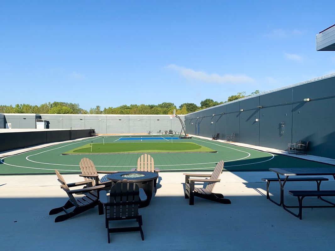 A patio with a table and chairs in front of a tennis court