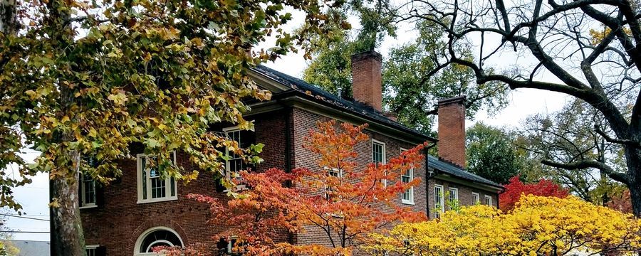 Brick house partly hidden by autumn trees with red, orange, and yellow leaves